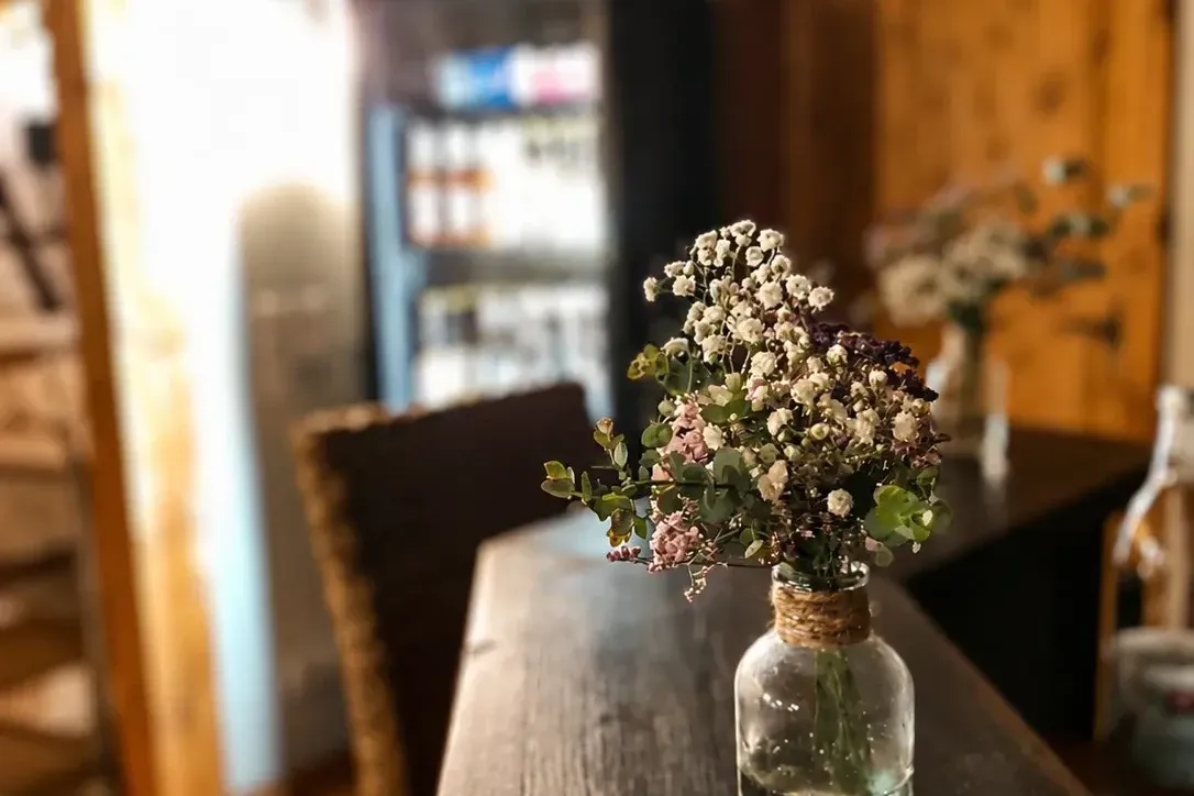 Wildblumenstrauß in Glasvase auf Holztisch, Getränkekühlschrank im Hintergrund