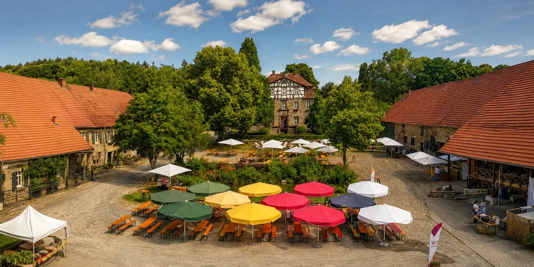 Innenhof von oben mit bunten Sonnenschirmen und Bierbankgarnituren beim Hoffest
