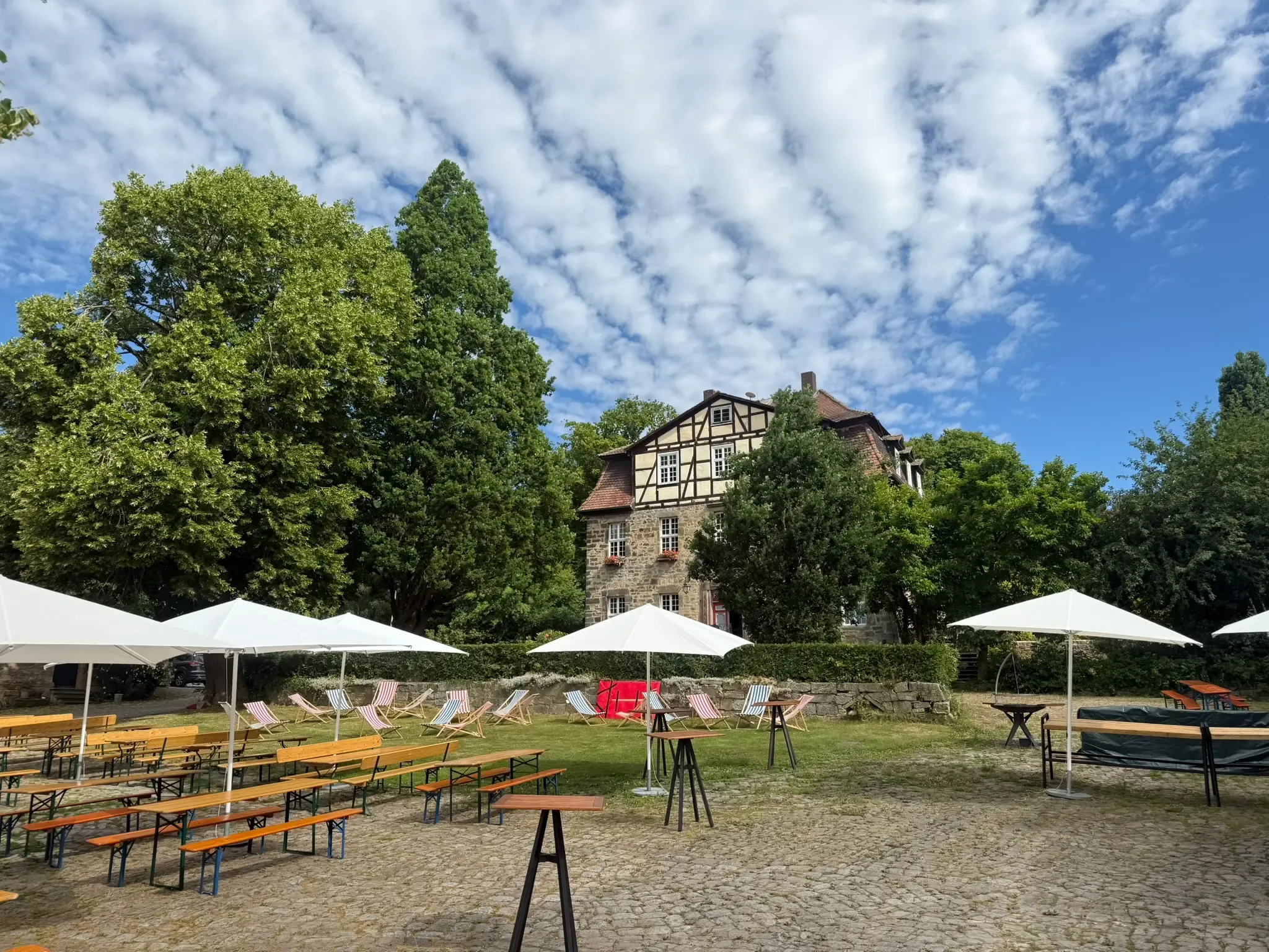 Außenbereich mit Sonnenschirmen, Bierbänken und Liegestühlen vor dem Gutshaus