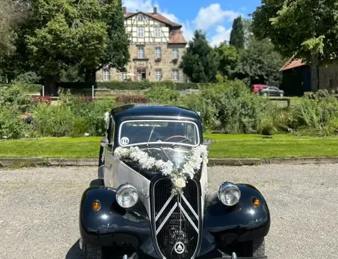 Schwarz-cremefarbener Oldtimer mit Blumenschmuck vor dem Gutshaus an einem sonnigen Tag